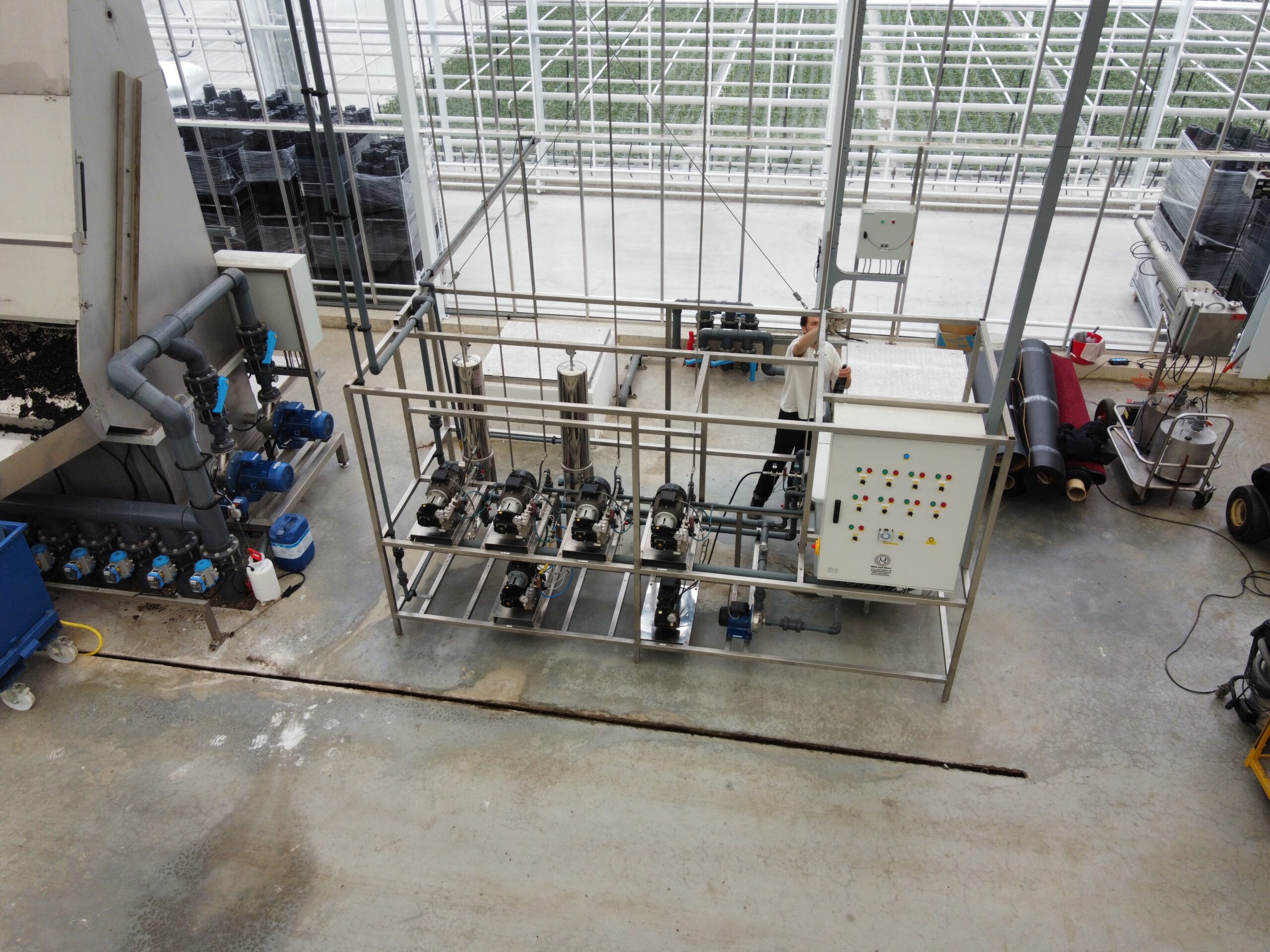 Doseerinstallatie met pompen en besturingskast in een kas, met gewassen op de achtergrond